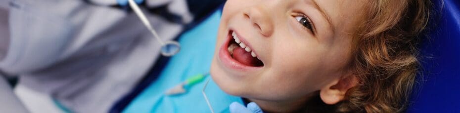 smiling child sitting in a blue chair dental